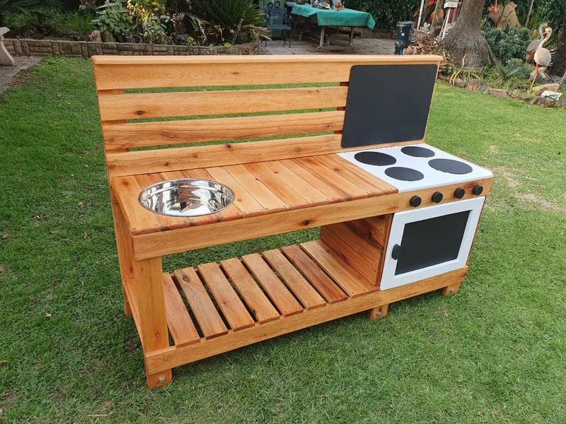 Wooden mud kitchen with a stainless steel bowl, painted hob and oven, slatted shelf and chalkboard.