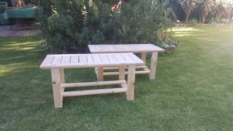 Two low wooden children's benches with slatted tops, splayed legs and long lower stretchers, standing on grass.