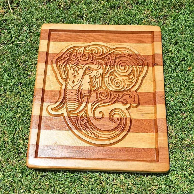 Striped wooden board with a raised border and a detailed elephant head carved into the centre.