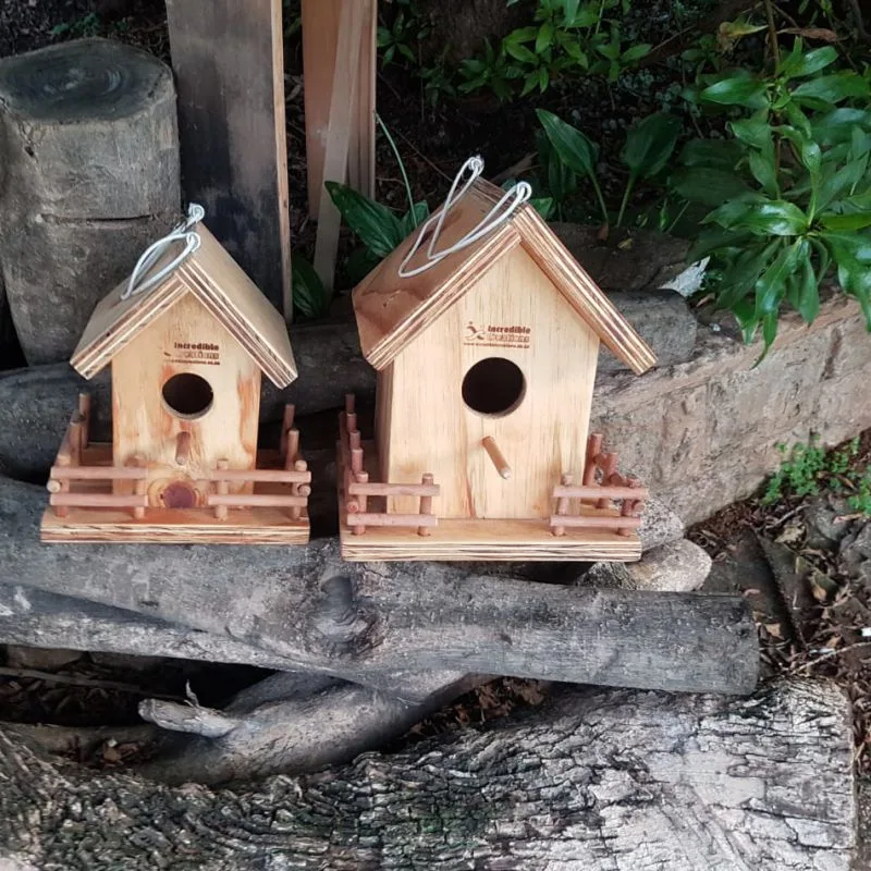 Two handmade wooden birdhouses with pitched roofs, round entrance holes, perches and small slatted fences.