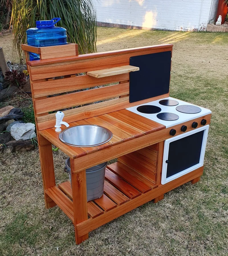 Wooden children's mud kitchen with stainless sink, tap, painted hob and chalkboard oven door.