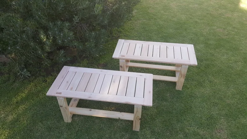 Two low child-height wooden benches with slatted seats and braced splayed legs, standing on grass.