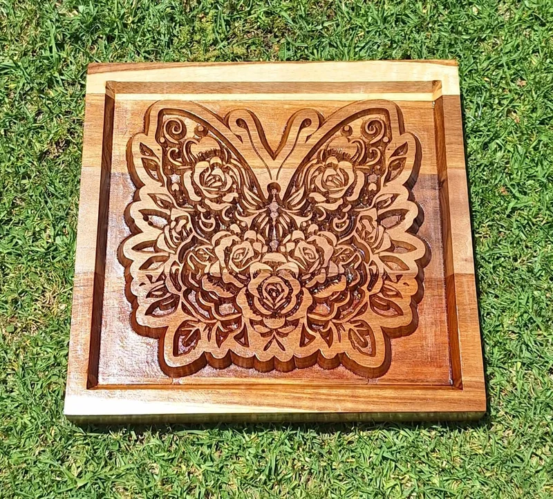 Square wooden panel with a butterfly and roses carved in relief inside a raised border.