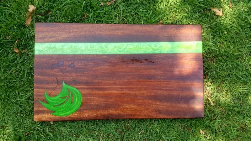 Rectangular dark wooden cutting board with a green resin stripe and a green resin leaf motif.