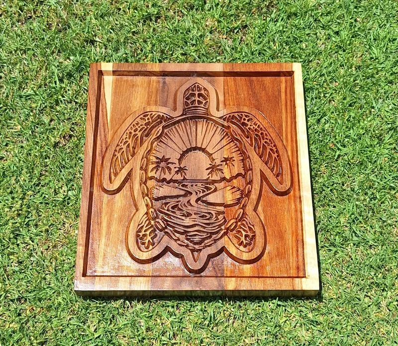 Square wooden panel with a sea turtle carved in relief, its shell showing a sun, palms and water.