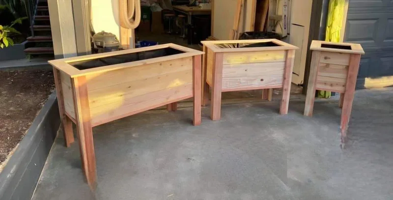 Three timber raised planter boxes on legs in long, square and narrow sizes, standing on a driveway.