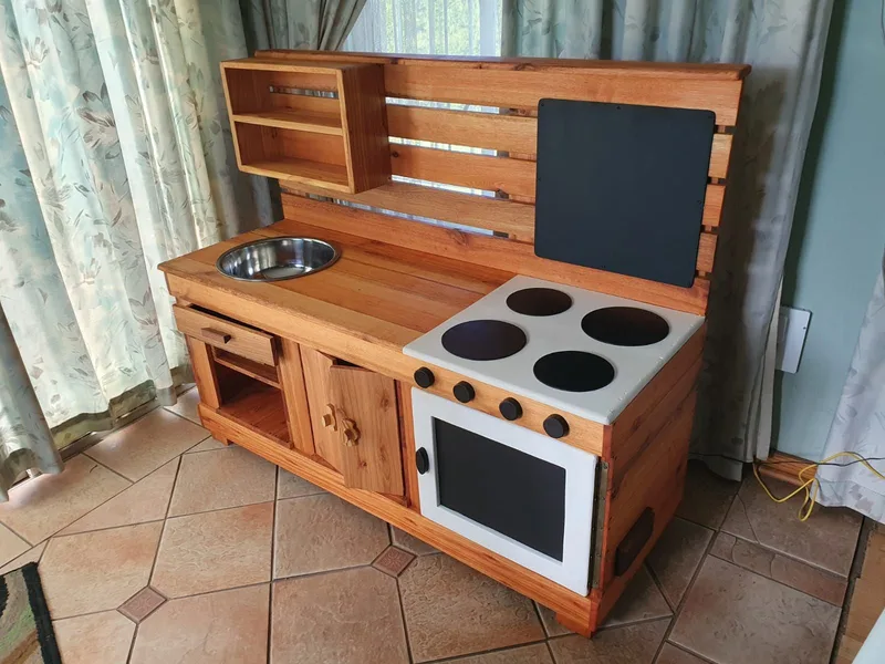 Wooden play kitchen with stainless sink bowl, painted four-plate hob, oven door, chalkboard and shelf.
