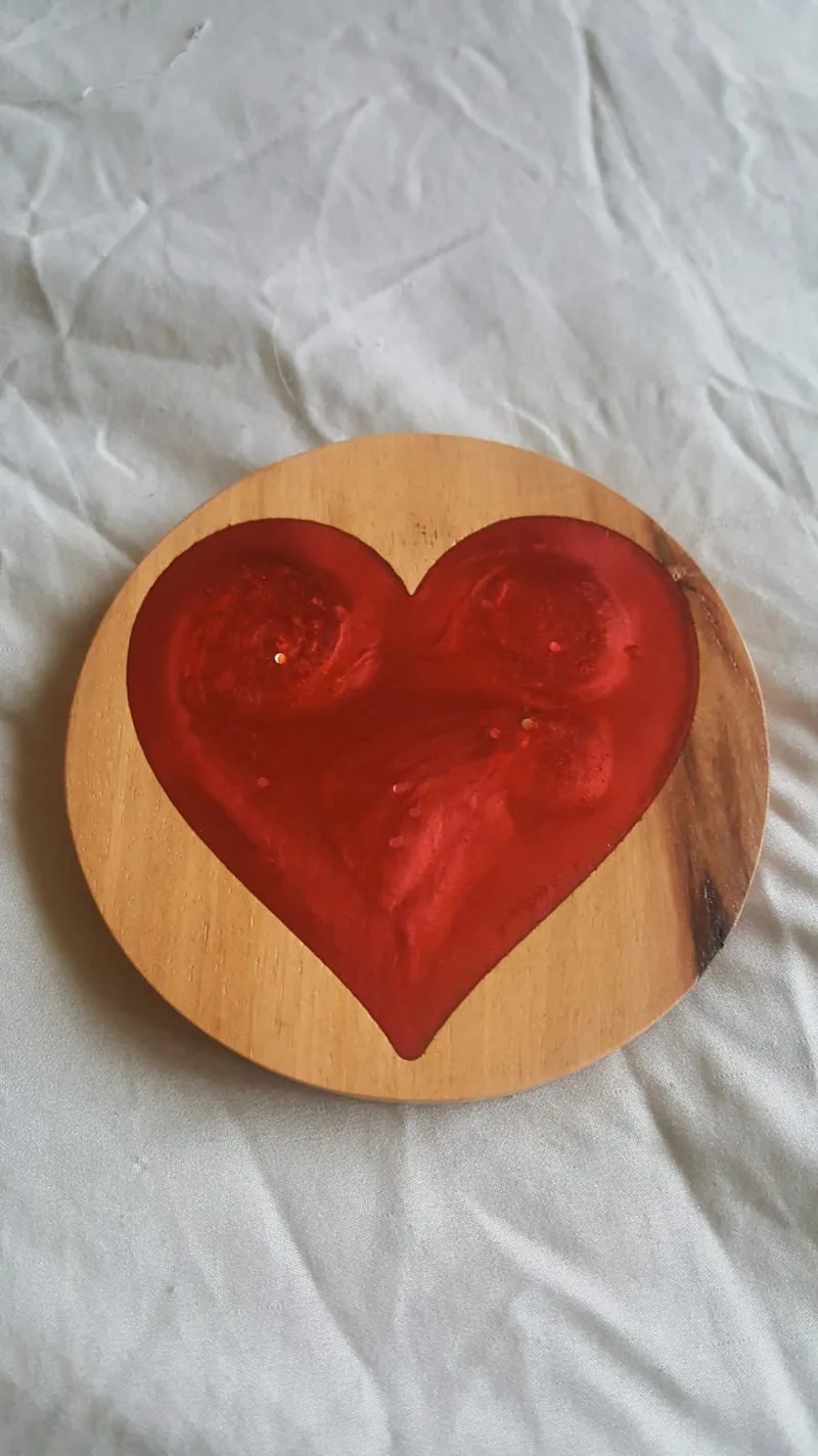 Round wooden coaster with a heart-shaped recess filled with red resin and one live edge.