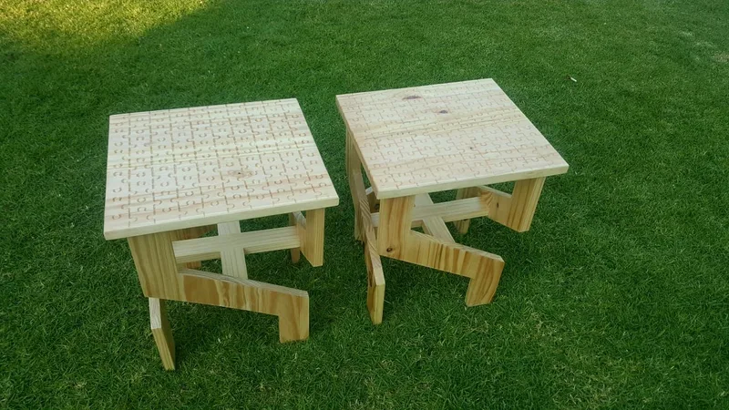 Two square light timber side tables on grass, each with a top made of small squares in a grid.