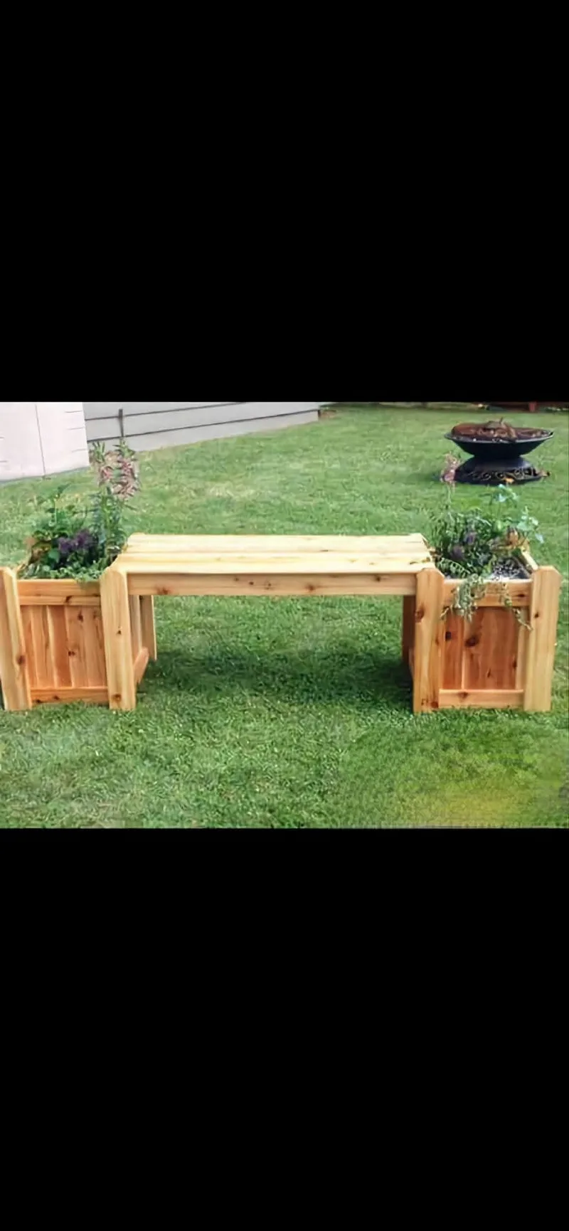 Wooden bench seat joined at both ends to square timber planter boxes holding plants, standing on grass.