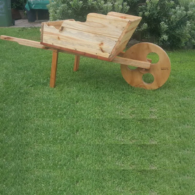 Handmade wooden wheelbarrow planter with slatted box, two handles and a solid timber wheel cut with round holes.