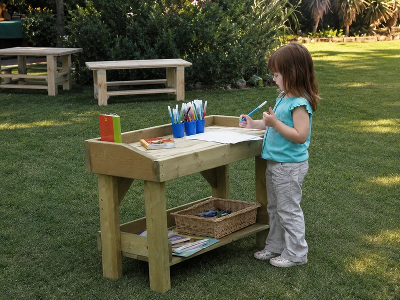 Wooden standing-height activity table with raised edges and a lower storage shelf, used by a young child.